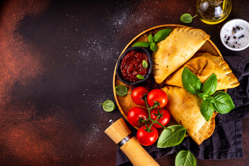 Homemade patty pies, baked pastries with meat or vegetables. Italian calzone closed pizza, Mexican empanada, Karaim Ukrainian pies. With homemade tomato sauce, basil greens and spices on dark table © ricka_kinamoto