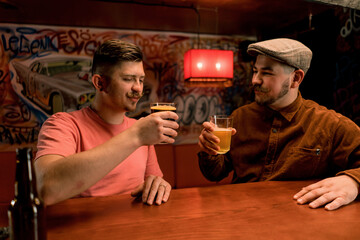 Two friends of a friend are sitting at the bar having fun talking and drinking beer in glasses in a...