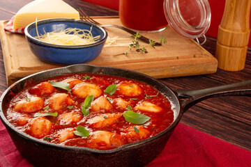 Delicious Gnocchi with Red tomato Sauce and Basil served in a black skillet pan in a red background in front view