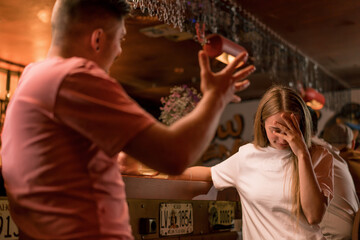 An upset guy with a mustache stands with a glass of beer in his hand at the bar and argues with a...