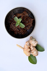 closeup the ripe maroon brown ginger with green mint leaves and brown chilly sauce in the metal bowl on the white background.