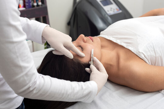 young woman on a table in a beauty center performing a beauty treatment for facial skin with the dermaplaning technique