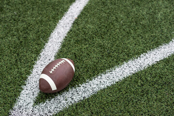 American football ball on green grass field background. Top view.