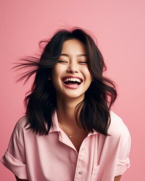 portrait of happy asian woman laughing on pink background