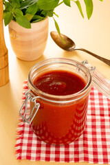 Fresh Tomato Sauce in a Glass Jar with basil leaves, sliced tomatoes in a beige background in front view