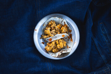 Breakfast chorizo and eggs tacos on a plate against a blue denim jacket