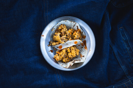 Breakfast chorizo and eggs tacos on a plate against a blue denim jacket