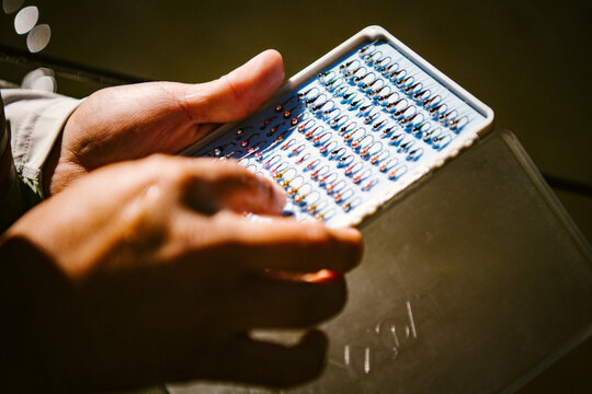 Hands hold a box of tiny fishing flies in the sun