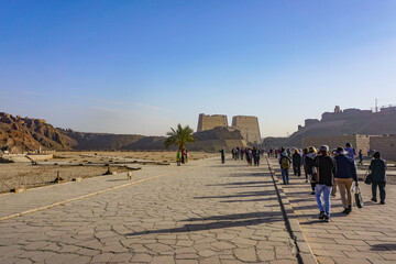 Edfu, Egypt: Visitors approach the entrance to the temple of Edfu, the largest temple dedicated to Horus and Hathor of Dendera, on a misty morning. - obrazy, fototapety, plakaty