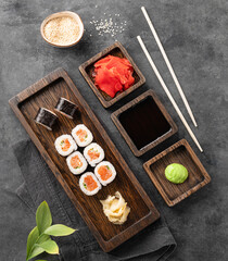 Set of rolls with raw salmon, rice and nori on a wooden board. Japanese sushi food concept with soy sauce, wasabi and ginger on a dark background.