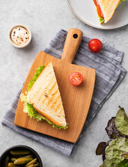 Club sandwich on a wooden board of ham, cheese, tomato and lettuce leaves on a blue background with mayonnaise.