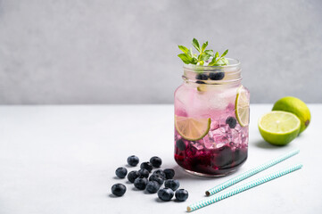 Blueberry mojito or lemonade with lime, ice and mint in a glass on a light background with berries, fruits anp papper tube. The concept of a summer refreshing drink.