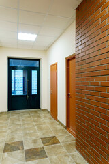 Obraz premium Decorative brick on the corridor wall in an office building. A black glass door at the end of the corridor of the business center. Interior design in the Art Nouveau style.