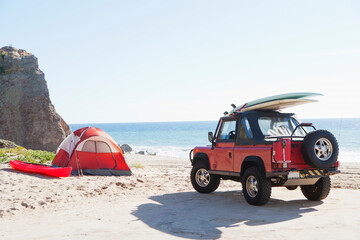 Red Jeep with surfboard at the beach next to camp tent