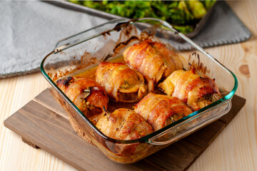 Baked honey-mustard chicken thighs with rosemary and wrapped in bacon. Roasted broccoli shown in the background.
