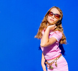 Attractive model Barbie style girl wearing sunglasses, pink tee-shirt and shorts with long hair on blue backdrop, vintage fashion concept. Hight quality photo