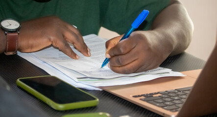 An immersive shot showing the steady hand of an African man, deliberately writing with a pen as he...