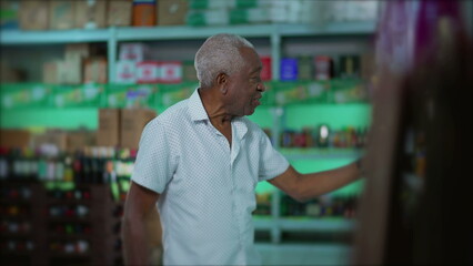 Candid elderly African American man selecting beverage from shelf at grocery store. One senior black male shopping for alcoholic drink at supermarket