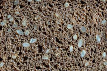 Abstract background or texture homemade black bread with sunflower seeds, closeup, top view, macro