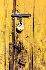 kłódka wisząca na zamkniętych starych żółtych odrapanych drewnianych drzwiach - obrazy, fototapety, plakaty