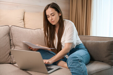 Naklejka premium Pretty young woman freelancing while checking documents