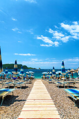 beautiful view of the sea beach, path to the sea, umbrellas and sun loungers, an island in the distance, Montenegro, the Adriatic Sea, tourism and summer travel