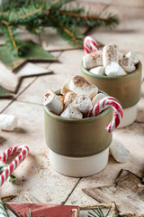 Holiday xmas food mug with hot chocolate cocoa and marshmallows decorated with candy canes with fir xmas tree branches on beige tile background. Happy New year celebration. Christmas fun