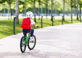 Happy ethnic child schoolboy in a helmet and with a briefcase rides a bike to school.