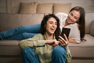 Two smiling women having fun using phone