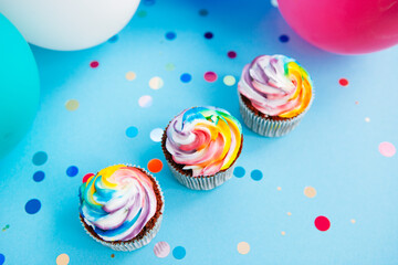 Three rainbow colors cupcake on blue background with air balloons from top view	