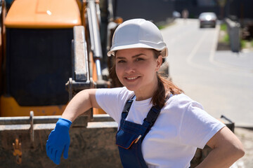 Smiling woman bulldozer operator leaning on bucket, resting