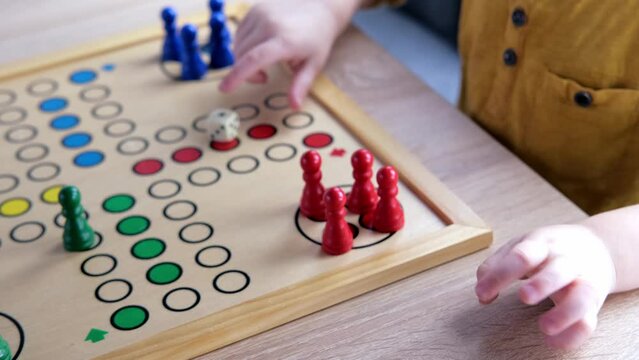 close-up of hands of small child manipulate with wooden figurines of family board game, smart kid, 2-year-old girl is learning to count, Cross and circle game Parcheesi, foreground focus