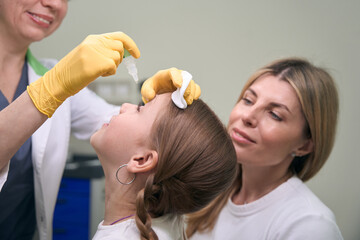 Doctor ophthalmologist instills medicine in the girls eye