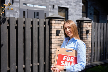 Realtor with a sign for sale looking at the camera