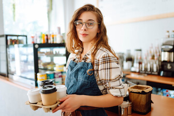 Portrait of a young woman barista holding takeaway coffee in her hands. Owner of the coffee shop...