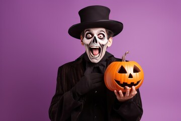 Man in Halloween costume. Skeleton in black cloak and top hat standing isolated on light purple background, holding orange jack o lantern