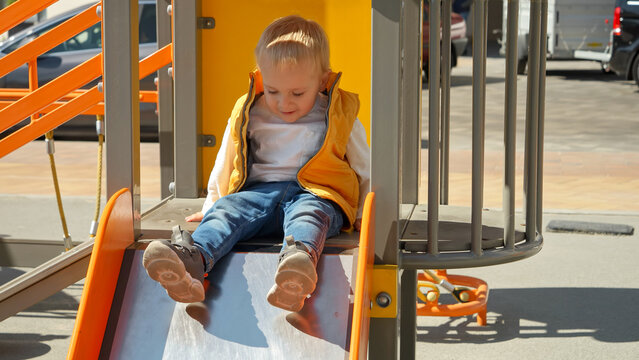 Little baby boy sitting on the top of the slide at playground and asking for help. Happy parenting, family having time together, kids and parents outdoors.