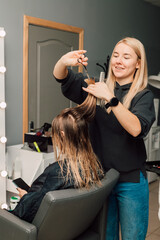 A hairdresser cuts a blonde's hair in a beauty salon. Women's haircut