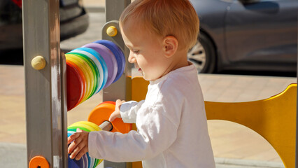 Happy smiling baby boy having fun on playground playing with colorful abacus. Children developments, kids education, baby learning.