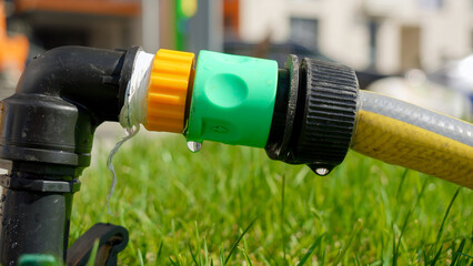 Water droplets leaking through damaged water hose pipe connection. Water waste, gardening equipment