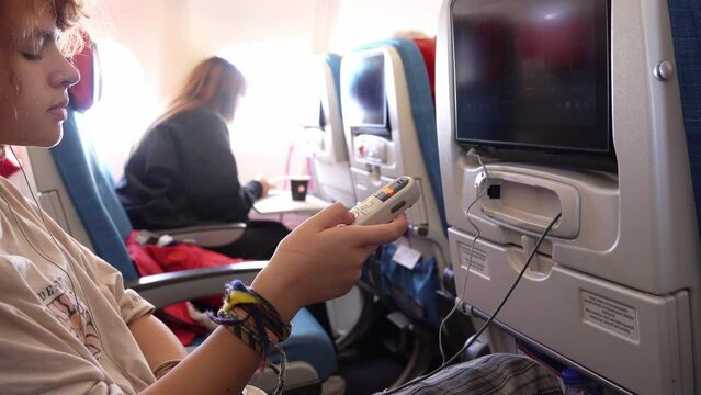 Young girl watching a movie on a plane on a entertainment screen using a remote control