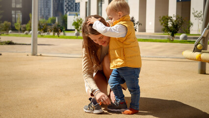 Little toddler boy holding mother while she is putting on him shoes on the playground