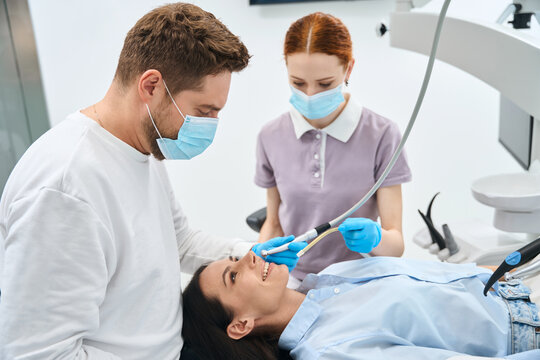 Professional dentist in uniform talking to female client during teeth treatment