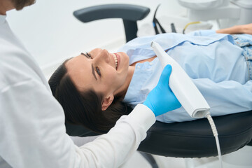 Woman lying in orthodontic chair, preparing for check-up with intraoral camera