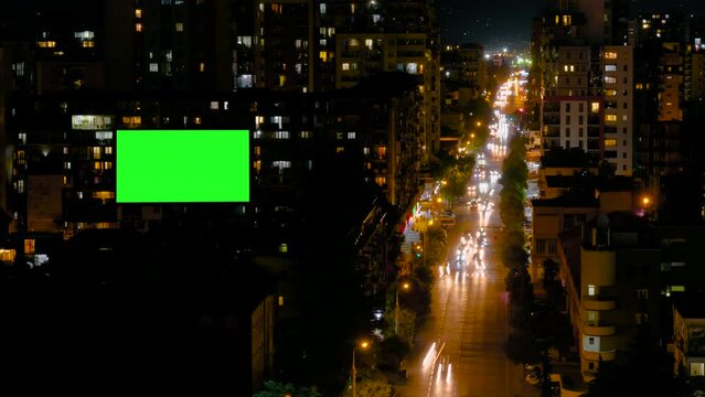Timelapse: blank green billboard or large display on building, fast moving car traffic and light trails in evening time with night illumination. Green screen, time lapse and copy space concept