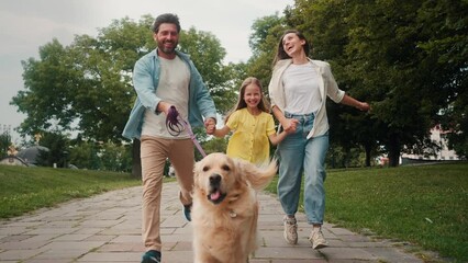 Happy parents and daughter run holding dog on leash in park
