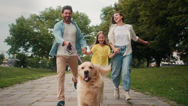 Happy parents and daughter run holding dog on leash in park