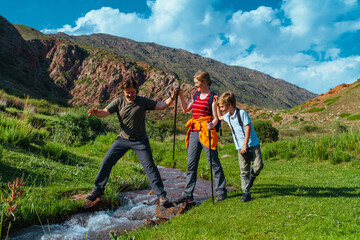 Parents hiking with their son across mountains stream - 628694740