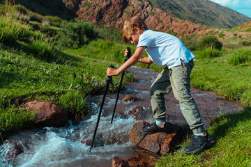 Boy with trekking poles checks the depth of mountain stream