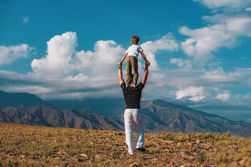 Boy standing on his father's shoulders on mountains background - 628694789